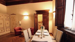 Un coin repas avec un parquet en bois disposé en chevrons, une table dressée pour quatre personnes avec des nappes et des assiettes blanches, et un fauteuil rouge.