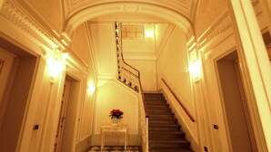 Un magnifique escalier, orné de balustrades travaillées et doté d’un sol à carreaux, mène à un palier où se trouve un vase rempli de fleurs.