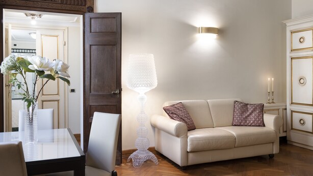 A living room with a glass table, a white sofa, a decorative floor lamp, and a cabinet with gold accents. - ARTWORK APARTMENT IN FLORENCE CITY CENTER (Firenze)