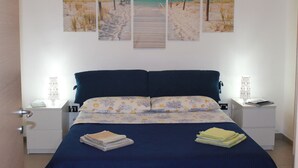 A bedroom with a bed, two bedside tables, a nightstand, and a wall with three beach-themed paintings. - Marina di Ragusa - House with garden (Santa Croce Camerina)