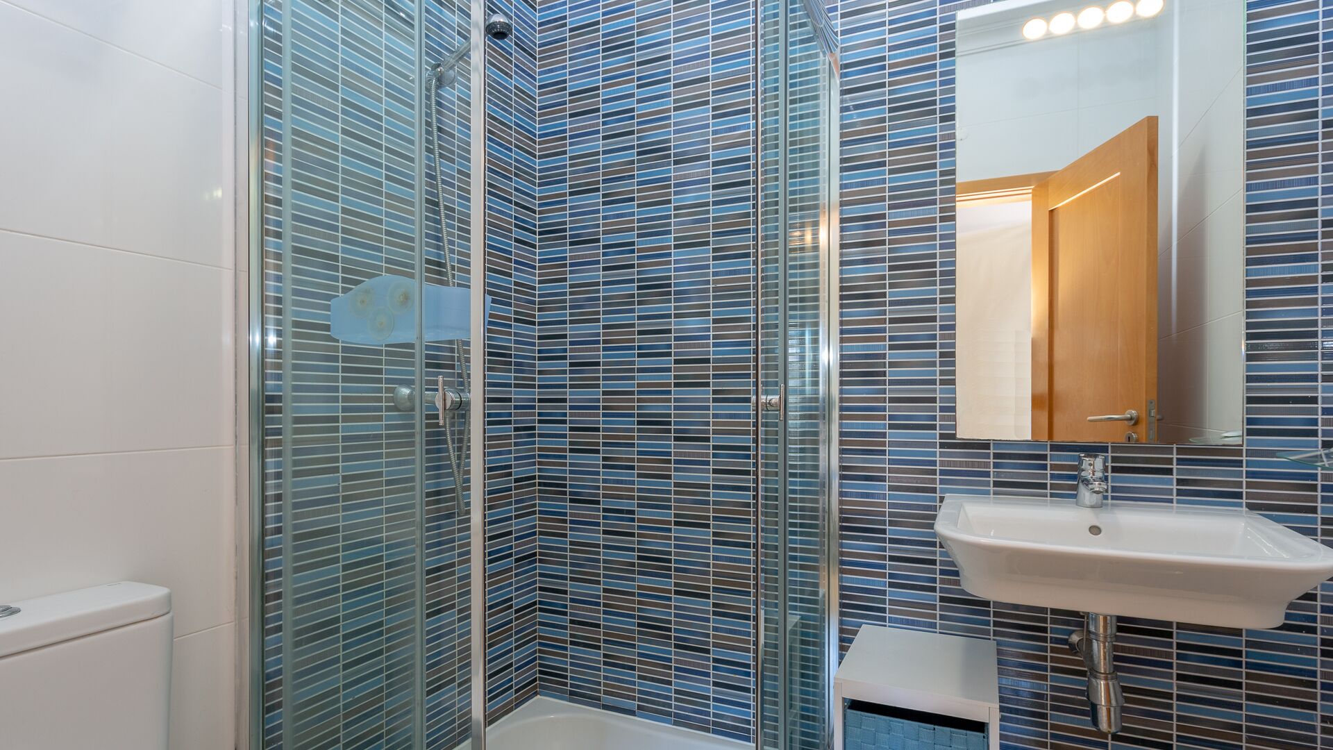 A bathroom with a glass shower enclosure, a white sink, and a mirror above it.