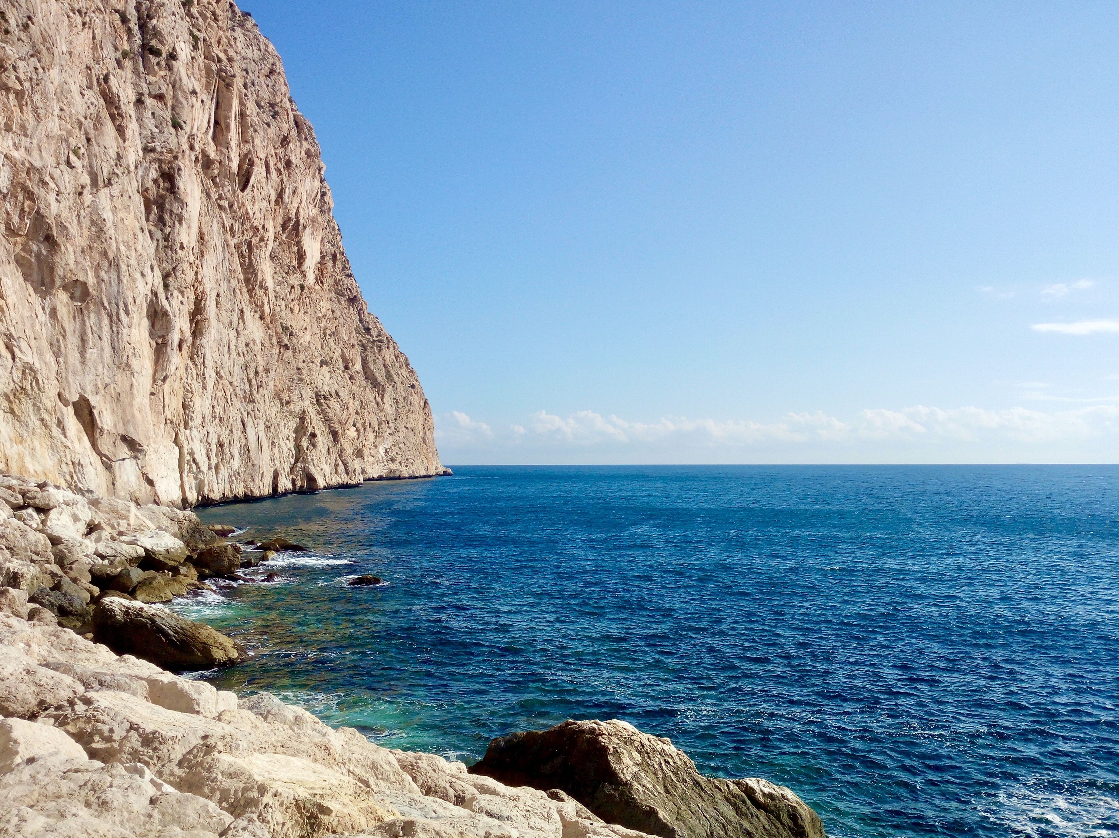 A coastal landscape with a prominent rocky cliff and clear blue sea.