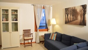 A living room with a blue sofa, a wooden chair, a cabinet with glass doors, a window with curtains, and a lamp.