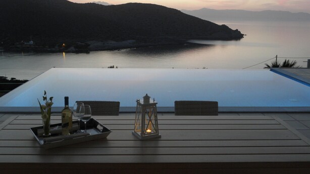Une terrasse offrant une vue sur une mer calme et les montagnes au crépuscule.