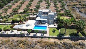 Une maison moderne à deux étages, dotée d’une piscine, entourée de jardins aménagés et de palmiers.