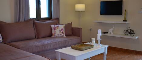 A living room with a sofa, a coffee table, a television, and a shelf with decorative items.