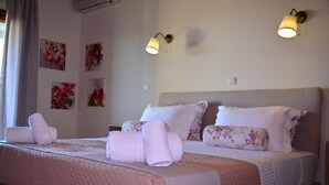 A neatly made bed with pink bedding and floral pillows, two wall-mounted lamps, and several floral artwork on the wall. - Elianthos Villas / Villa Rose 🌹 (Chania)