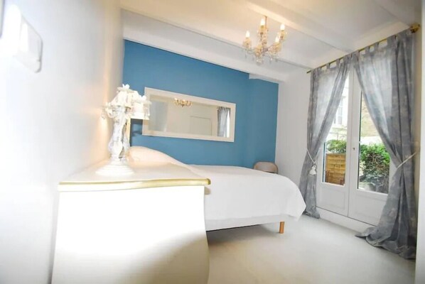 A bedroom with a bed, a dresser, a mirror, a chandelier, and a window with curtains.