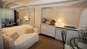 Ett kompakt hotellrum med en vit soffa, ett litet matbord och ett litet pentry.