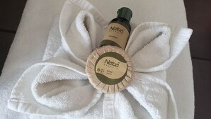 Une serviette blanche sur laquelle sont posés un flacon de shampoing Natuá Organic et un savon.