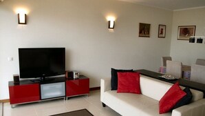 Una sala de estar moderna con un televisor de pantalla plana, sillones de acento rojo y negro, un sofá blanco y una mesita de centro rojo y negro.