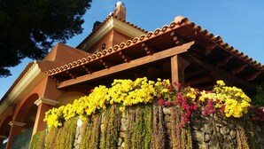 A building with a stone wall and a wooden pergola covered with yellow and pink flowers. - .First line luxrury villa. No car needed ,Tram stop 1 minute walking. (El Campello)