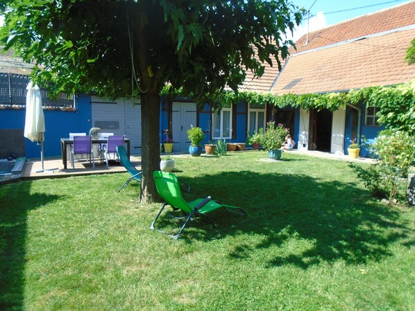 Une cour avec une pelouse, un arbre et un espace patio aménagé avec des chaises et une table.