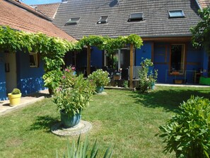 Une cour agrémentée de plantes en pot, un espace aménagé avec des sièges et un bâtiment doté d’un toit recouvert de tuiles.