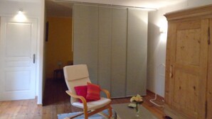 A room with a wooden floor, a white door, a white chair with a red cushion, a wooden cabinet, and a sliding closet door. - To explore the Christmas Markets in Alsace! (Neuf-Brisach)