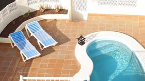 Una piscina con dos sillones azules y un farol.