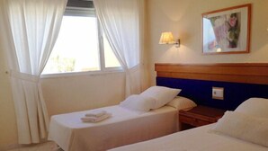 Una habitación de hotel con dos camas individuales, una mesita de noche de madera, una lámpara y una ventana con cortinas.