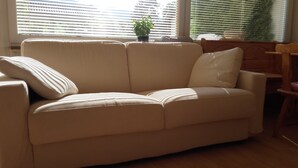 Un sofá color beige con almohadas a rayas en una habitación con ventana y persianas.