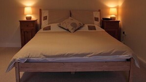 A bed with a wooden frame, two bedside tables with lamps, and a single pillow with a floral design. - Lovely renovated Stone Cottage & Garden, great location Central Yorkshire (TADCASTER)