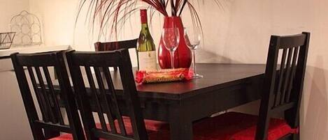 A dining table with four black chairs, each with red cushions. A red vase with long, dark red feathers and a wine bottle are on the table.