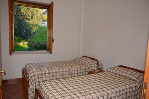 Un dormitorio con dos camas, una ventana con vistas a zonas verdes y una mesita de noche pequeña.
