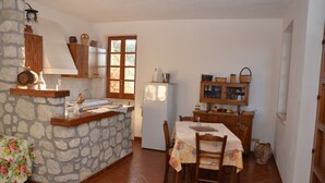 Une cuisine avec des murs en pierre, des meubles de rangement en bois, une table à manger avec des chaises et un réfrigérateur.