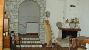Un intérieur rustique avec une arche en pierre menant à un escalier, une cheminée avec un manteau en bois et un coin repas avec des meubles en bois.