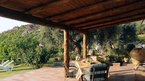 Une terrasse extérieure dotée d’une pergola en bois, d’un sol en pierre et d’une table avec des chaises.