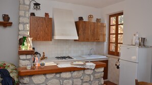 Une cuisine avec des murs en pierre, des meubles de rangement en bois, une cuisinière à gaz et un réfrigérateur.