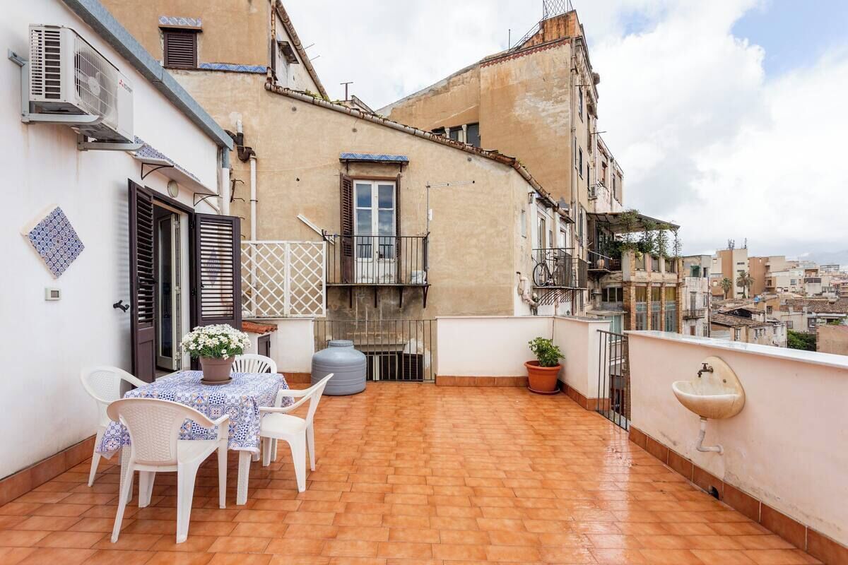 A rooftop terrace with a table and chairs, a potted plant, a water tank, and a sink.