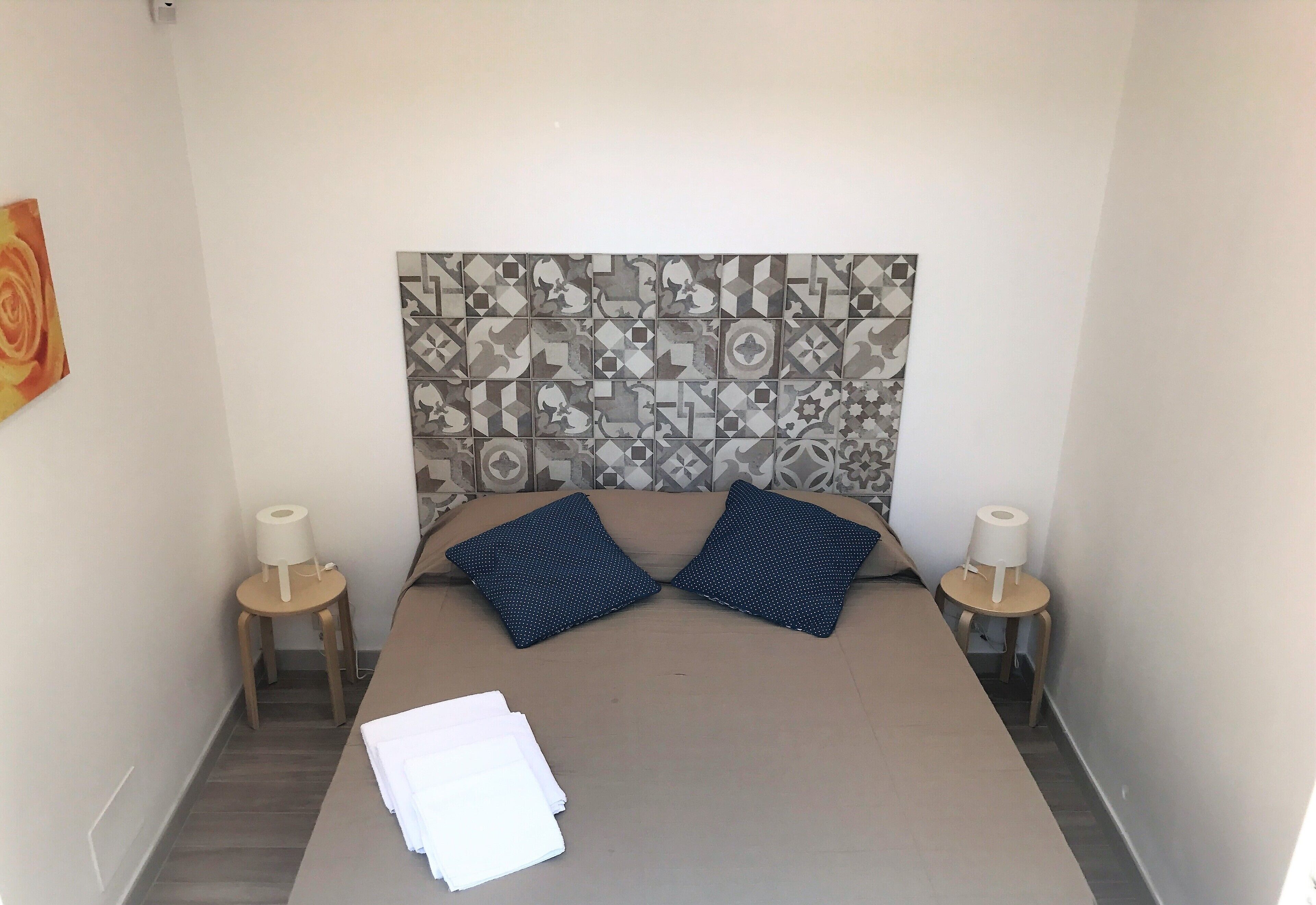 A neatly made bed with a patterned headboard, two pillows, and a stack of white towels on the floor.