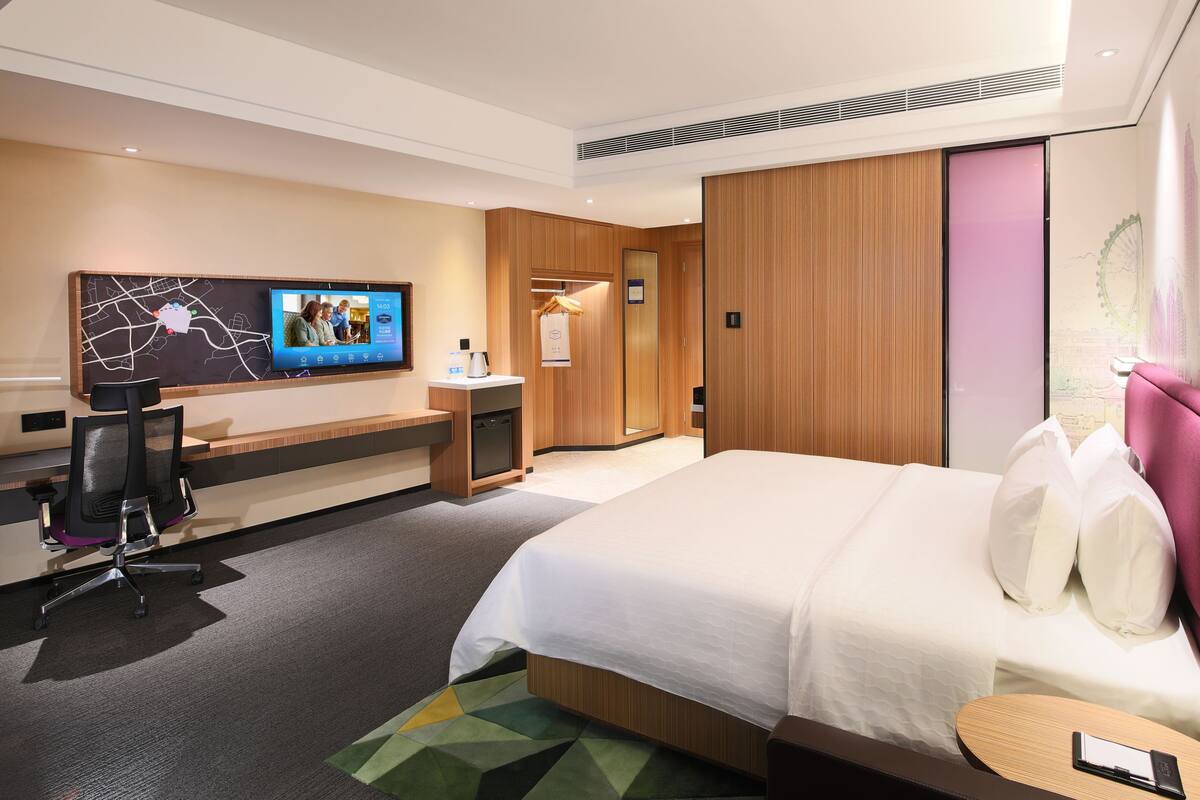 Una habitación de hotel con cama, escritorio, silla, televisor y armario.
