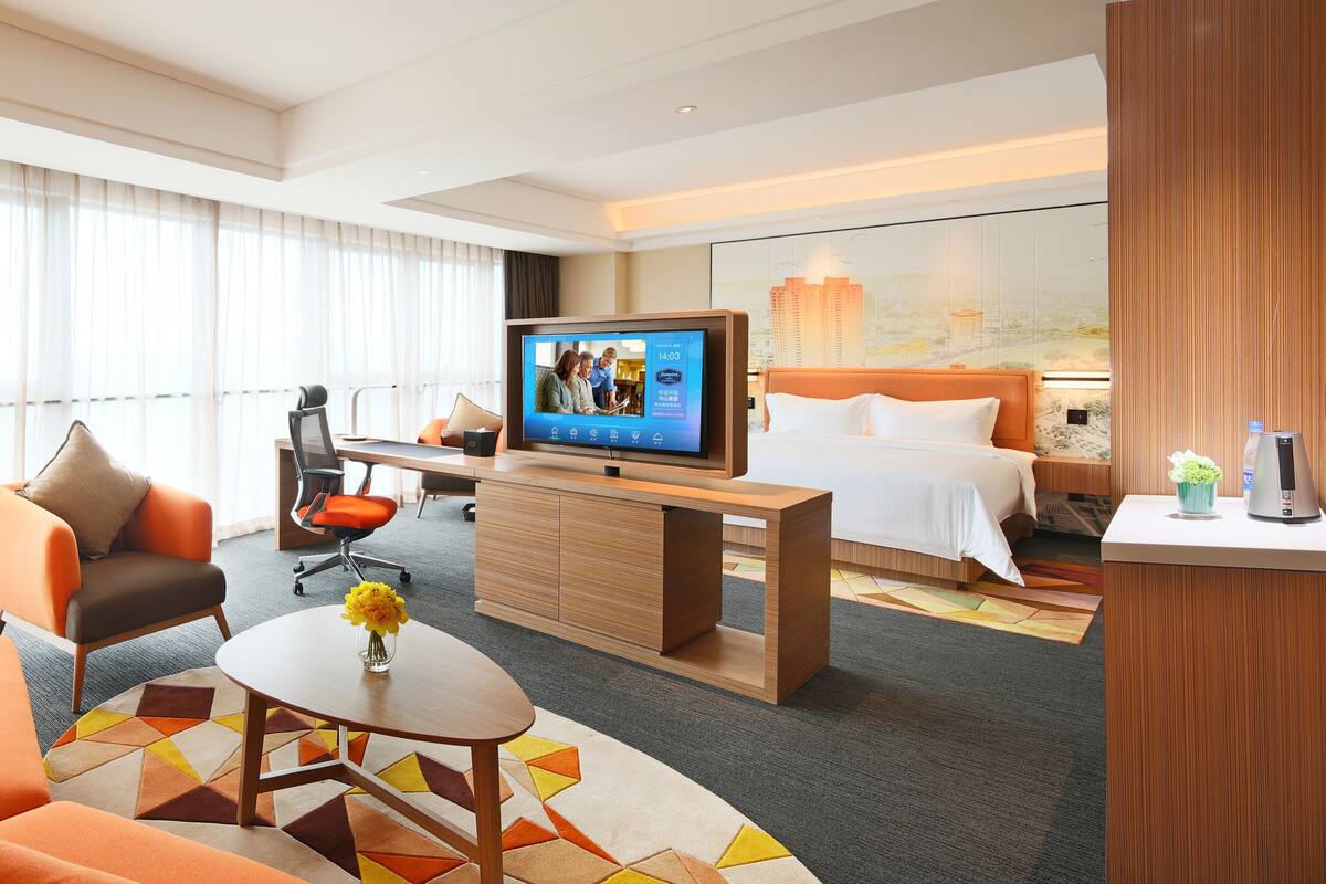 Una habitación de hotel con cama, televisión, escritorio, silla, sofá y lámpara.