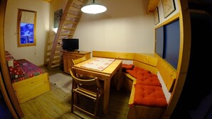 Une chambre confortable dans un chalet, avec un plafond en bois, un lit en mezzanine, une table à manger et un téléviseur.