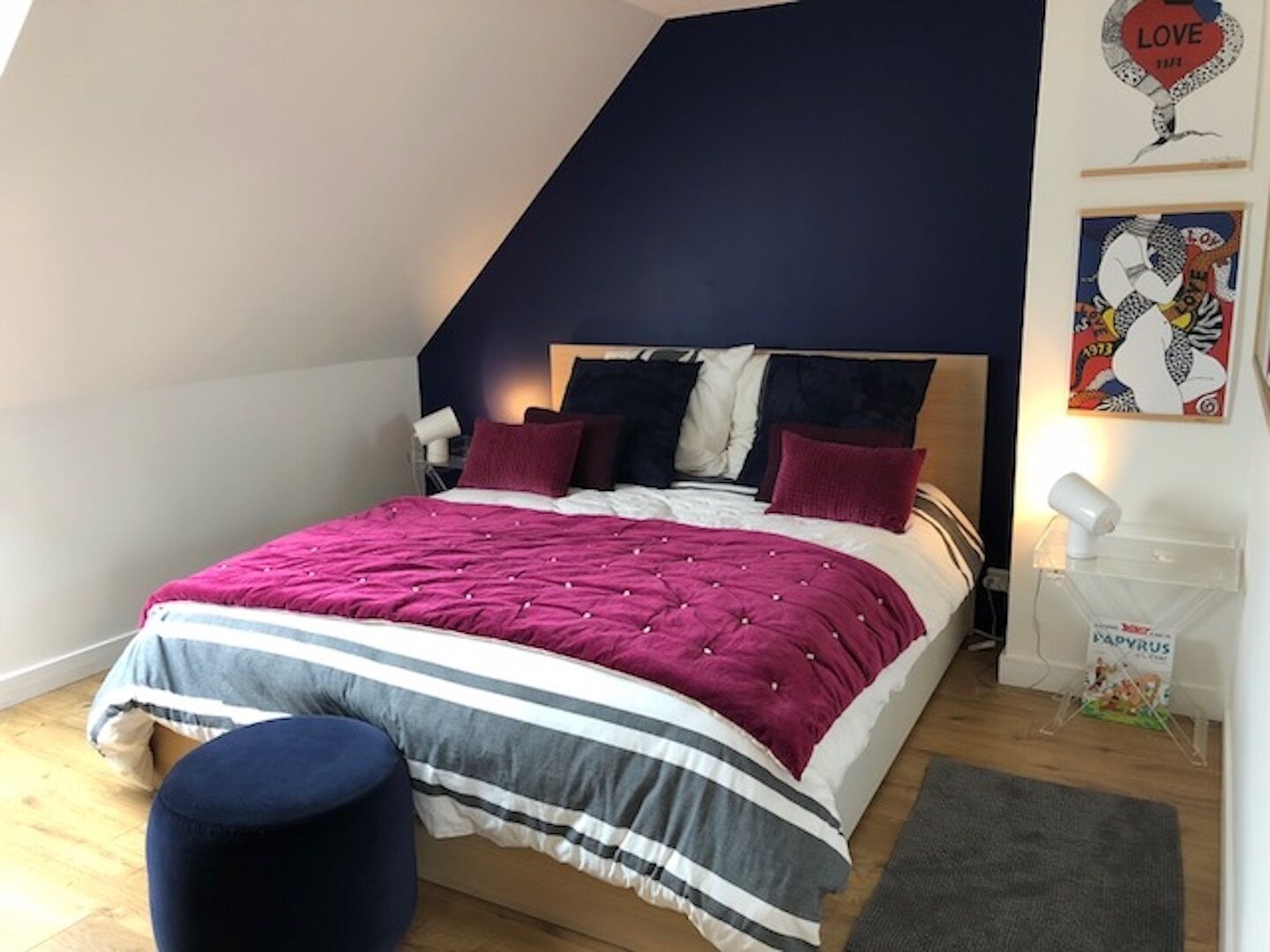 A bedroom with a sloped ceiling, a bed with a pink and white striped bedspread, and a dark blue accent wall.