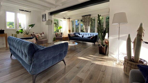 A spacious living room with a blue sofa, a dark blue sofa, and a coffee table. There are large windows with curtains, a floor lamp, and a cactus plant. - 4 BEDROOM HOUSE FOR 2 to 6 PEOPLE (La Forêt-Fouesnant)
