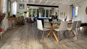 A modern dining area with a glass table and white chairs, a blue sofa, and a chandelier. - 4 BEDROOM HOUSE FOR 2 to 6 PEOPLE (La Forêt-Fouesnant)