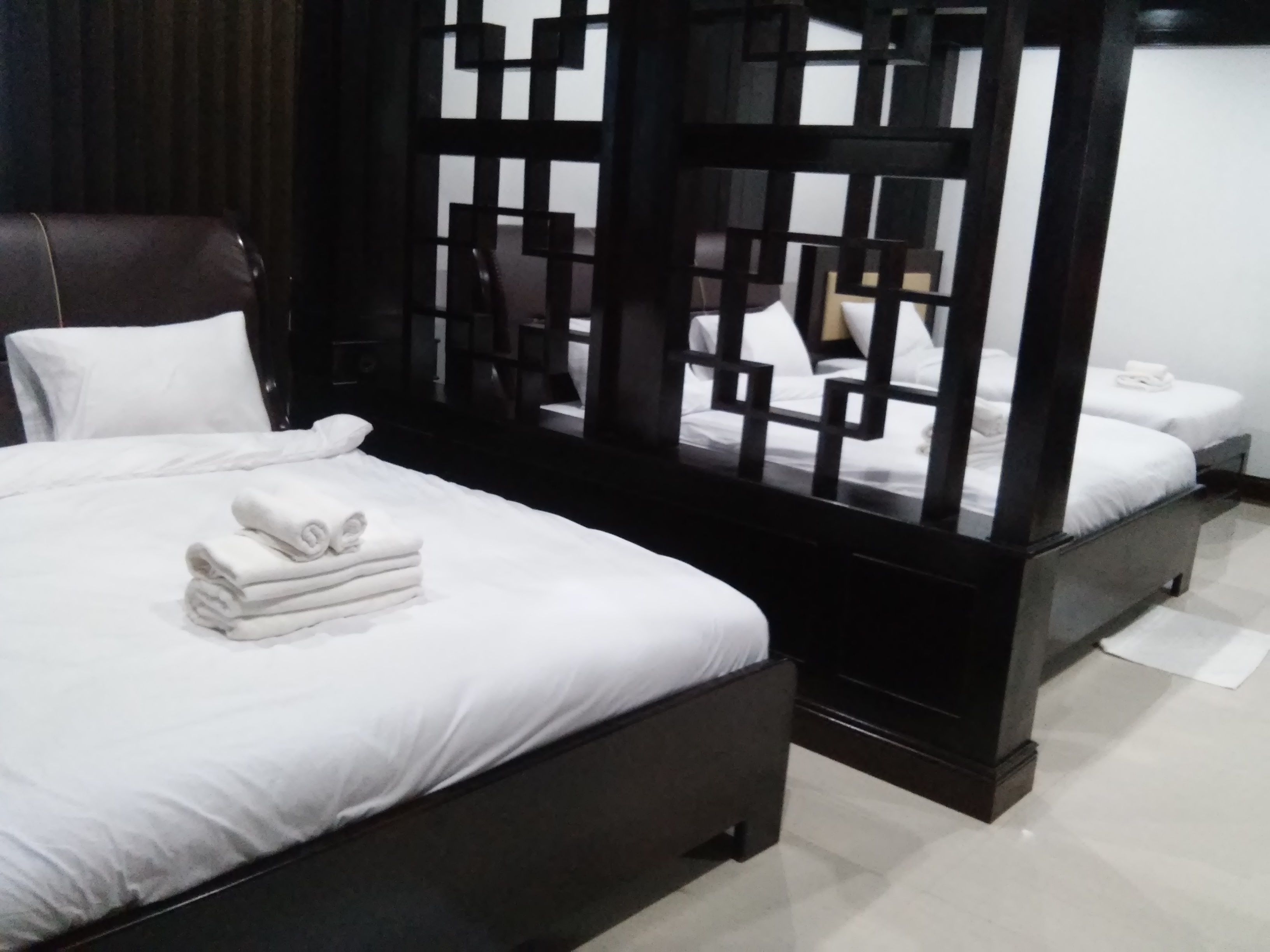 A modern hotel room with a large bed, a separate sitting area, and a view through a geometric partition.