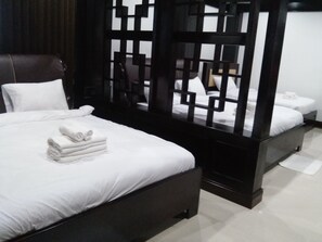 A modern hotel room with a large bed, a separate sitting area, and a view through a geometric partition.