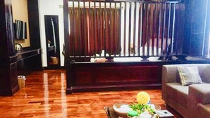 Una sala de estar con piso de madera, un sofá, una mesa de centro con un jarrón de flores y un televisor sobre un mueble.