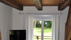 Ein Zimmer mit Holzbalkendecke, einem Fernseher auf einer Holzkommode, einem Bett mit weißer Bettwäsche und einer Glastür, die zu einem Außenbereich führt.