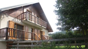 Un chalet en bois à deux étages, doté de balcons, de murs en pierre et d’une clôture en bois.
