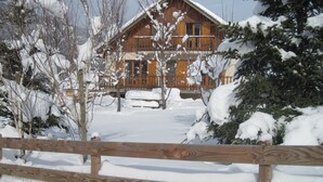 Une cabane en bois dotée d’un porche, entourée d’arbres couverts de neige.