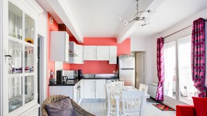 Une cuisine moderne avec des meubles blancs, une table à manger avec des chaises, un canapé en osier et un fauteuil rouge.