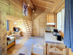 A wooden interior with a bed, desk, TV, and kitchen area. - Small chalet with breathtaking views of Mont-Blanc, 5 minutes from the ski slopes (Sallanches)