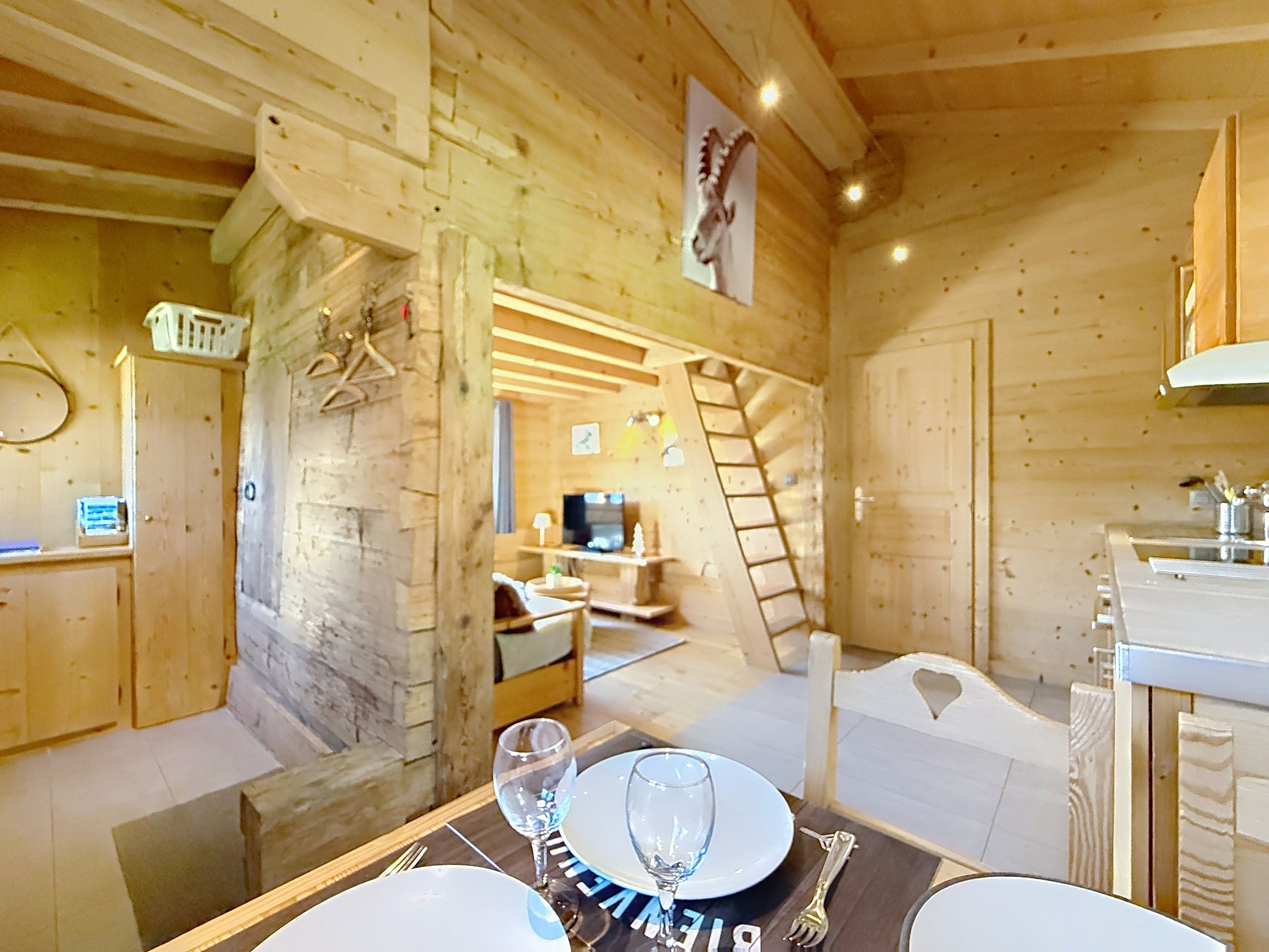 A wooden interior with a dining table set for two, a ladder, and a mounted picture.