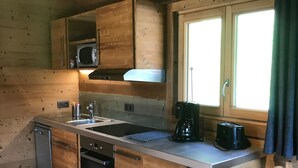 Uma cozinha compacta com armários de madeira, micro-ondas, cafeteira e janela com cortinas.