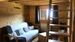 Interior de uma cabana de madeira com sofá, uma mesa pequena e uma escada.