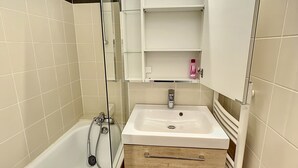 A modern bathroom with a bathtub, a sink, and a mirror. There are shelves above the sink and a glass shower enclosure. - Standing Apartment 4 people + Parking + Ski locker - Arcs 1800 (Bourg-Saint-Maurice)