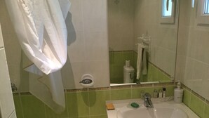 Un baño con lavamanos, espejo y paredes de azulejos verdes.